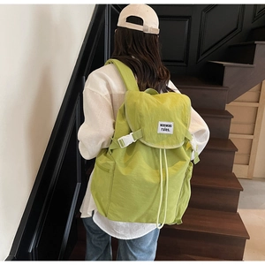 Rear view of a light green canvas backpack with white buckle and drawstring closure