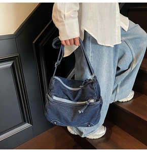 Close-up of deep blue denim crossbody bag featuring multiple zippers and metal rivets