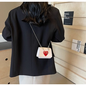 Detail of a mini cream PU crossbody bag with a red heart and silver chain strap