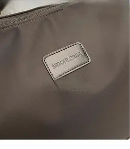 Detail of a dark brown nylon bag featuring a Moonlersa brand rectangular leather logo patch