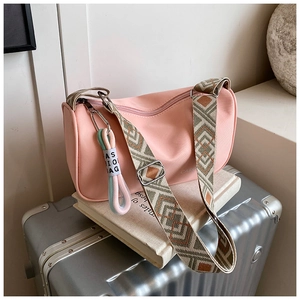Détail du sac cylindrique rose avec large bandoulière géométrique sur valise argentée