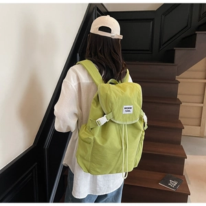 Close-up of light green nylon backpack with flap closure and white buckle detail