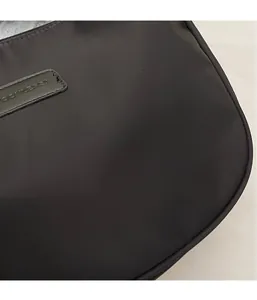 Detail of water-resistant black nylon fabric and stitched leather logo on crossbody bag
