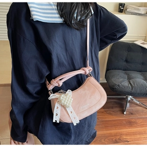 Detail of pink crossbody bag with a lace bow, pearl heart charm and knotted top handle