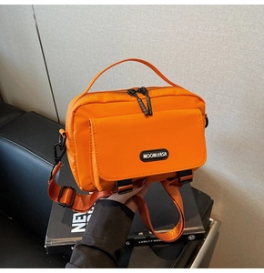 Detail view of bright orange waterproof nylon messenger bag with buckle and brand logo