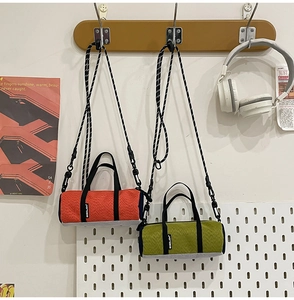 Close-up of orange and green mini cylinder crossbody bags with textured fabric and straps