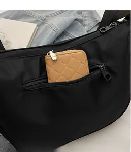 Close-up of black nylon crescent bag featuring a front zipper pocket with a brown wallet