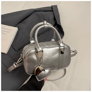 Close-up of a silver matte Boston bag with a heart pendant next to a grey blazer
