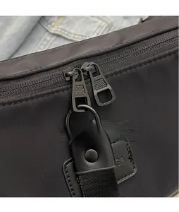 Close-up of dual smooth hardware zippers with leather pulls on black nylon crossbody bag