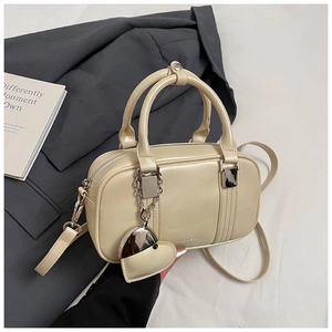 Close-up of beige bowling bag with RO&SK embossing and a metallic heart-shaped pendant
