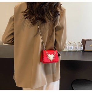 Detailed view of mini red PU leather crossbody bag with heart detail on a model