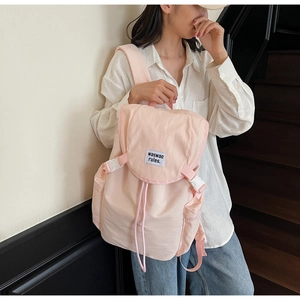 Close-up of pink canvas backpack with buckle closure and embroidered slogan detail