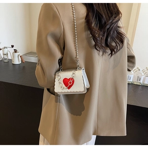 Detail of silver mini chain bag with red heart accent and floral metal strap elements