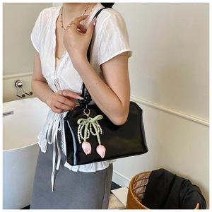 Detail of black glossy shoulder bag with elegant pearl tulip pendant accessory