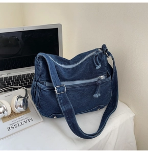 Detail of blue denim crossbody bag featuring zippers and adjustable strap with silver hardware