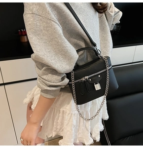 Detail of black pebbled leather vanity bag with silver lock and chain strap on model
