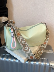 Sac bandoulière croissant vert clair avec sangle tissée sur une valise argentée