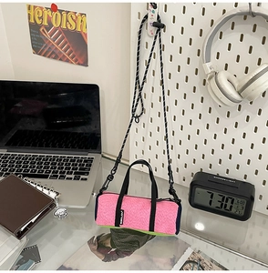 Mini running crossbody bag in pink and green colors on a desk with tech accessories