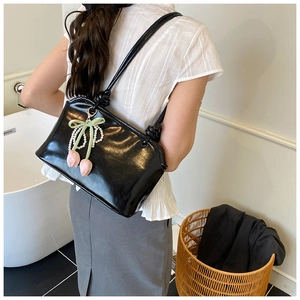 Detail of black patent leather tote bag with pearl bow and pink tulip charm on shoulder