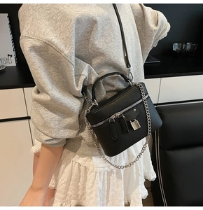 Model wearing a black litchi texture vanity crossbody bag with silver chain and padlock