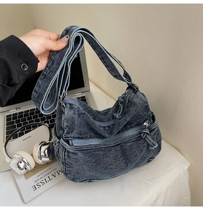 Detail of blue washed denim tote bag showing multiple zipper pockets and wide shoulder strap