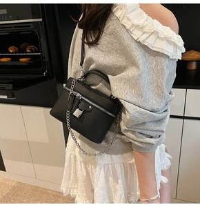 Detail of black litchi grain box bag with silver chain and padlock on a model in a kitchen