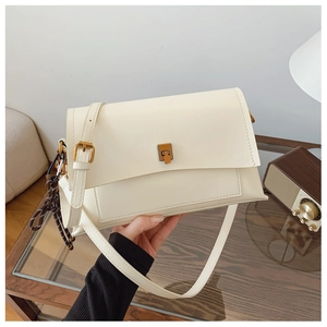 Détail du sac bandoulière en cuir blanc crème avec boucle dorée et breloque tressée