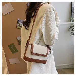 Detail of crossbody bag with beige canvas, brown leather trim and metallic BAIKOU logo