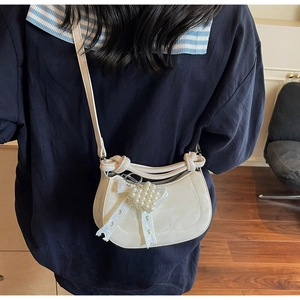 Detail of off-white half-moon crossbody bag with pearl heart and lace bow charm