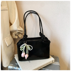 Detail of a black glossy tote bag featuring a tulip pearl charm and sleek patent leather finish