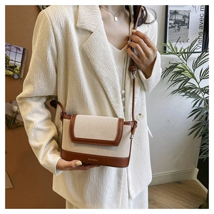 Model wearing a two-tone canvas and brown leather crossbody bag over a white blazer