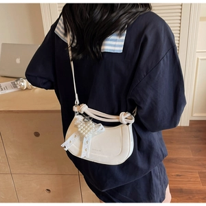 Detail of white half-moon bag featuring pearl heart charm and ribbon on model