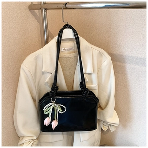 Detail of glossy black shoulder bag with pearl tulip charms on white blazer