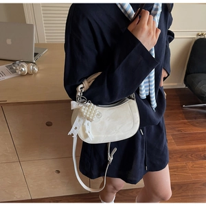 White crescent leather shoulder bag with pearl bow charm in a cozy indoor office setting