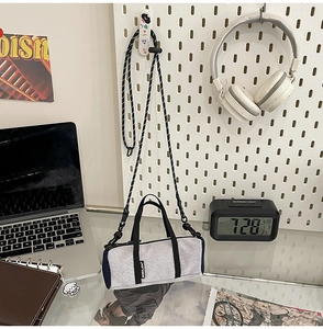 Close-up of a grey cylindrical crossbody bag with a blue mesh pocket and woven strap