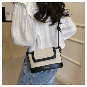 Close-up of canvas crossbody bag featuring black leather trim and gold brand logo