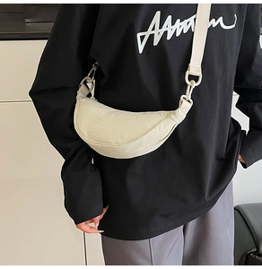Detail of beige crescent crossbody bag with wide shoulder strap worn by model