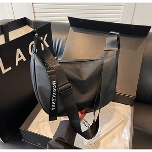 Detail view of the wide woven strap and logo ribbon on the black nylon crescent bag