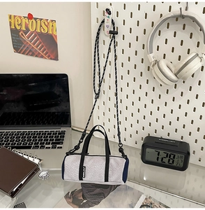 Close-up of grey mini bolster bag with mesh detail and adjustable strap on a modern desk
