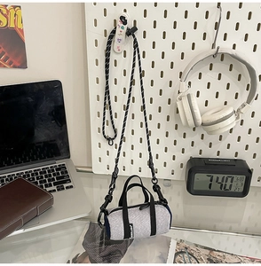 Mini grey knitted cylinder crossbody bag with striped strap shown in a lifestyle desk setting