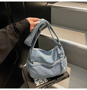 Detail of light blue denim tote bag with dual front zippers and metal base studs