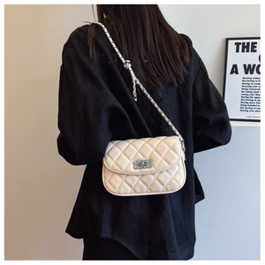 Detail of cream quilted crossbody bag with silver chain strap shown on model shoulder
