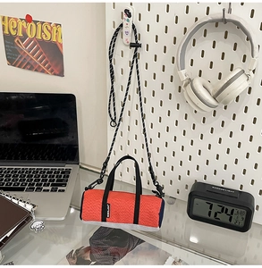 Close-up of a mini cylindrical sports crossbody bag in orange and blue on a desk