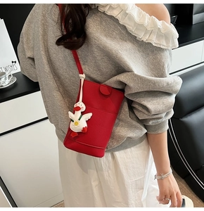 Red lychee leather crossbody bucket bag featuring a cute white duck charm accessory