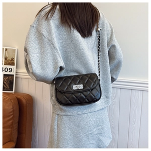 Detail view of a black quilted crossbody bag with silver chain strap on a model