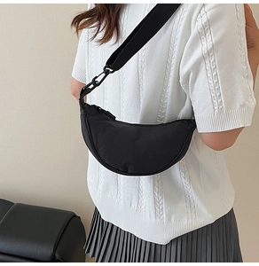 Chic black nylon crescent crossbody bag styled with a white knit sweater and pleated skirt