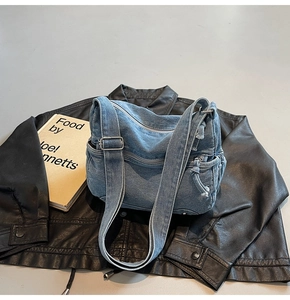 Detail of light blue denim crossbody bag with multiple zippers over a leather jacket