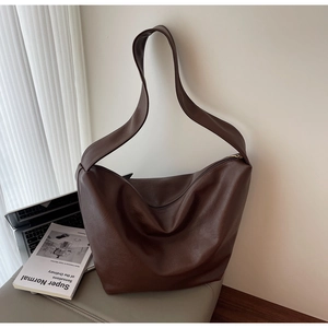 Detail of soft dark brown pebble leather shoulder bag next to a laptop and design book