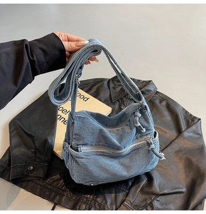 Detailed view of blue denim crossbody bag with multiple zippers and knotted pulls