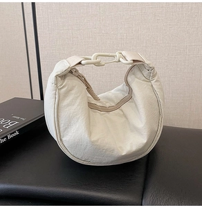 Detail of cream nylon dumpling bag showing pleated texture and plastic buckle strap closure